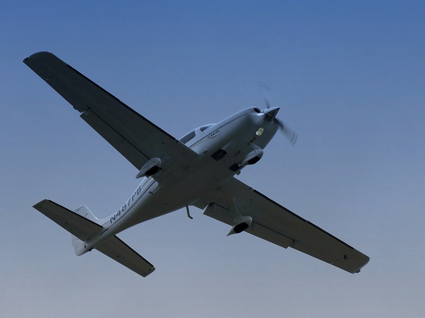 A Cirrus SR22 in a steep diving bank against a deep blue sky, propeller spinning